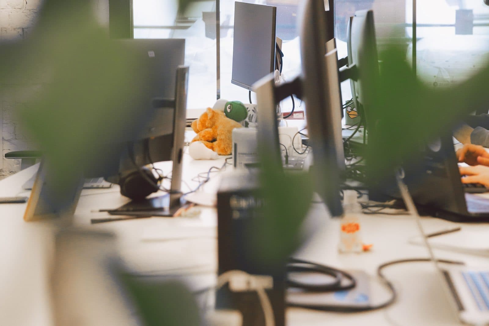 A row of developer desks with monitors and hardware in a bright open-plan engineering office, someone working at the far end