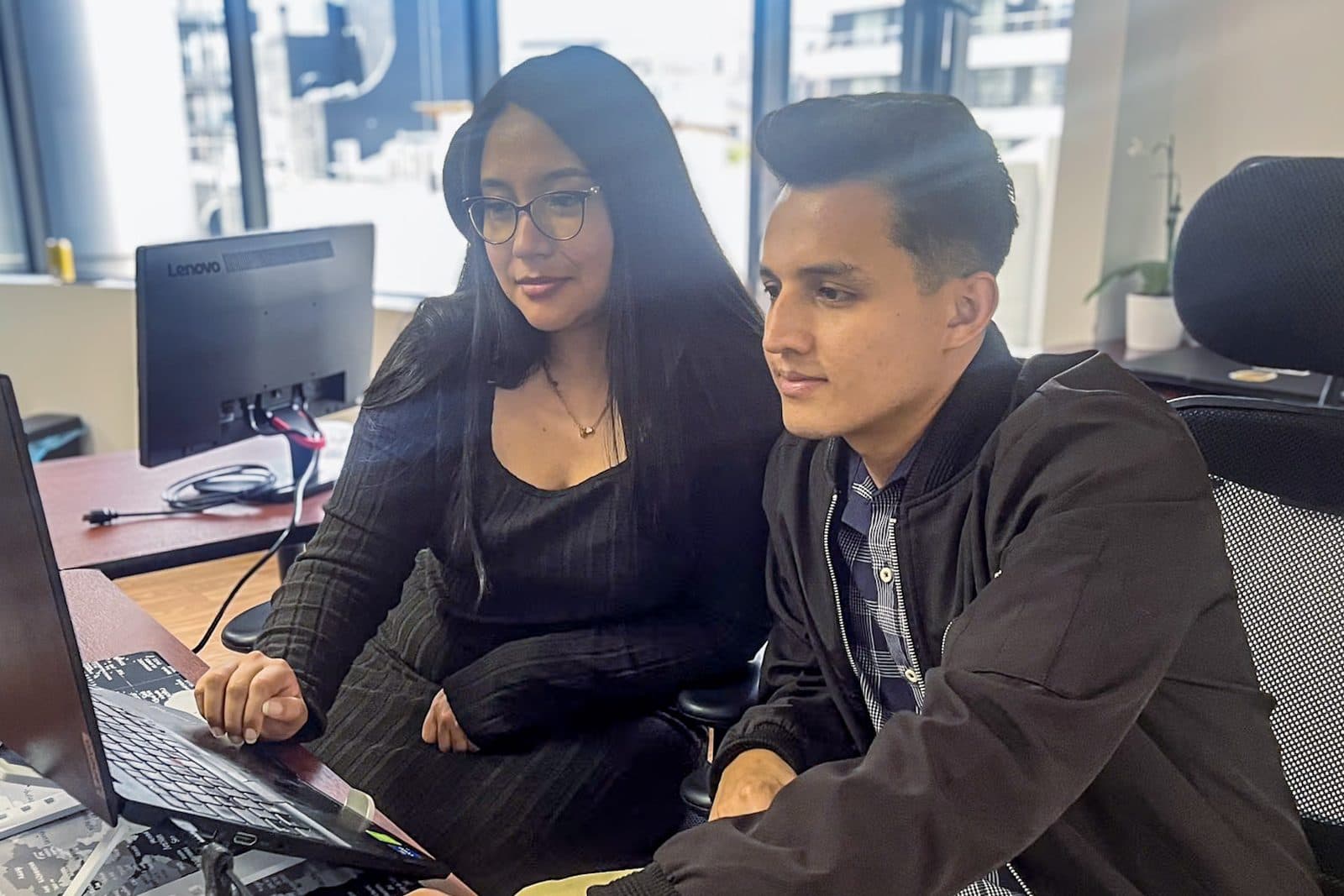 Two Senirop developers reviewing code together at a shared workstation in the Quito, Ecuador office