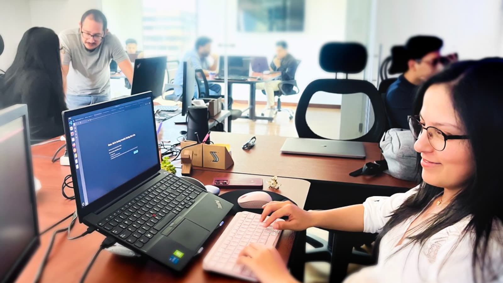 Senirop strategic advisory consultant working at a laptop in the Quito office, with teammates collaborating in the background